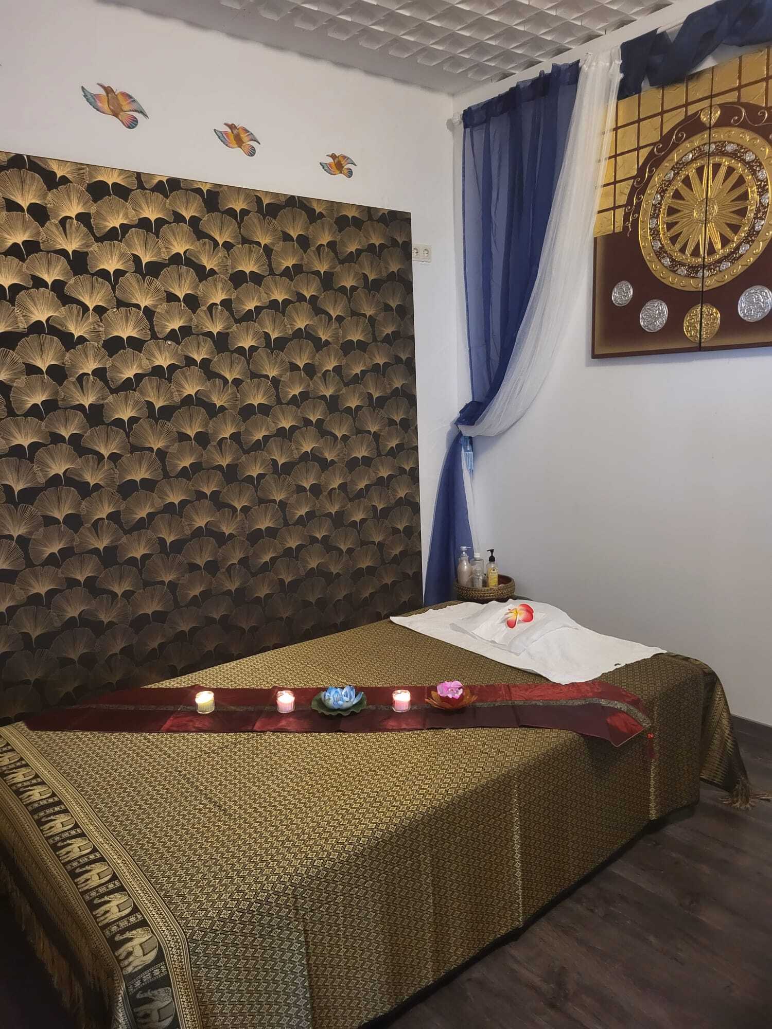 Elegantes Thai-Massagezimmer mit dekoriertem Massagetisch, Kerzen, Blüten und entspannender Atmosphäre